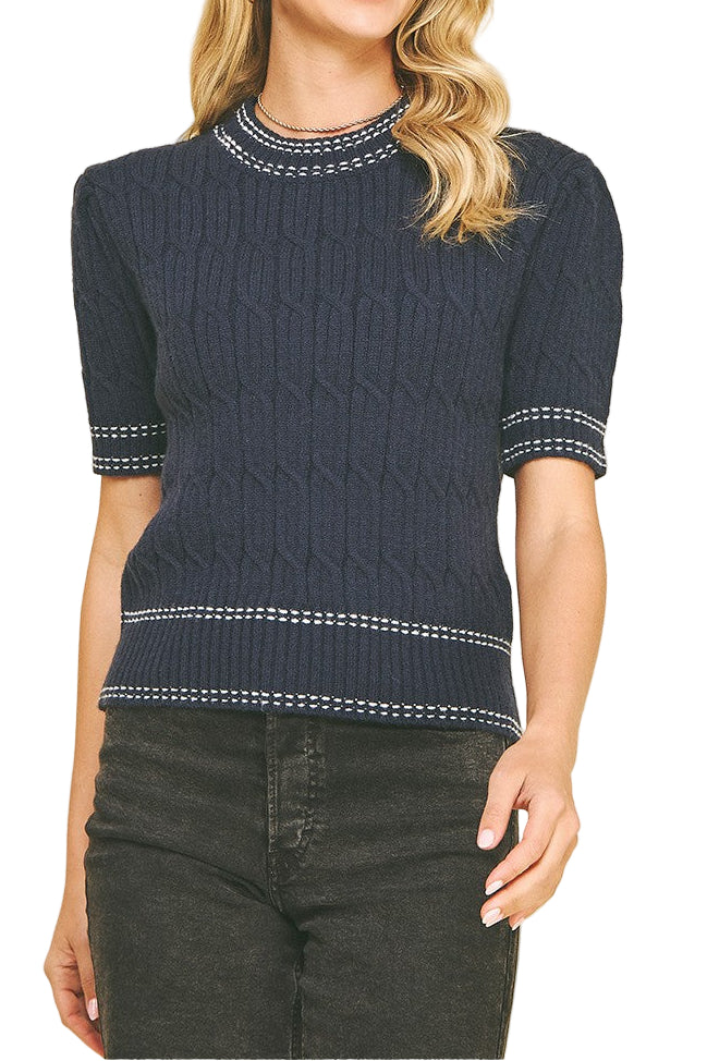 Woman wearing a navy blue sweater with white trim on a beige background
