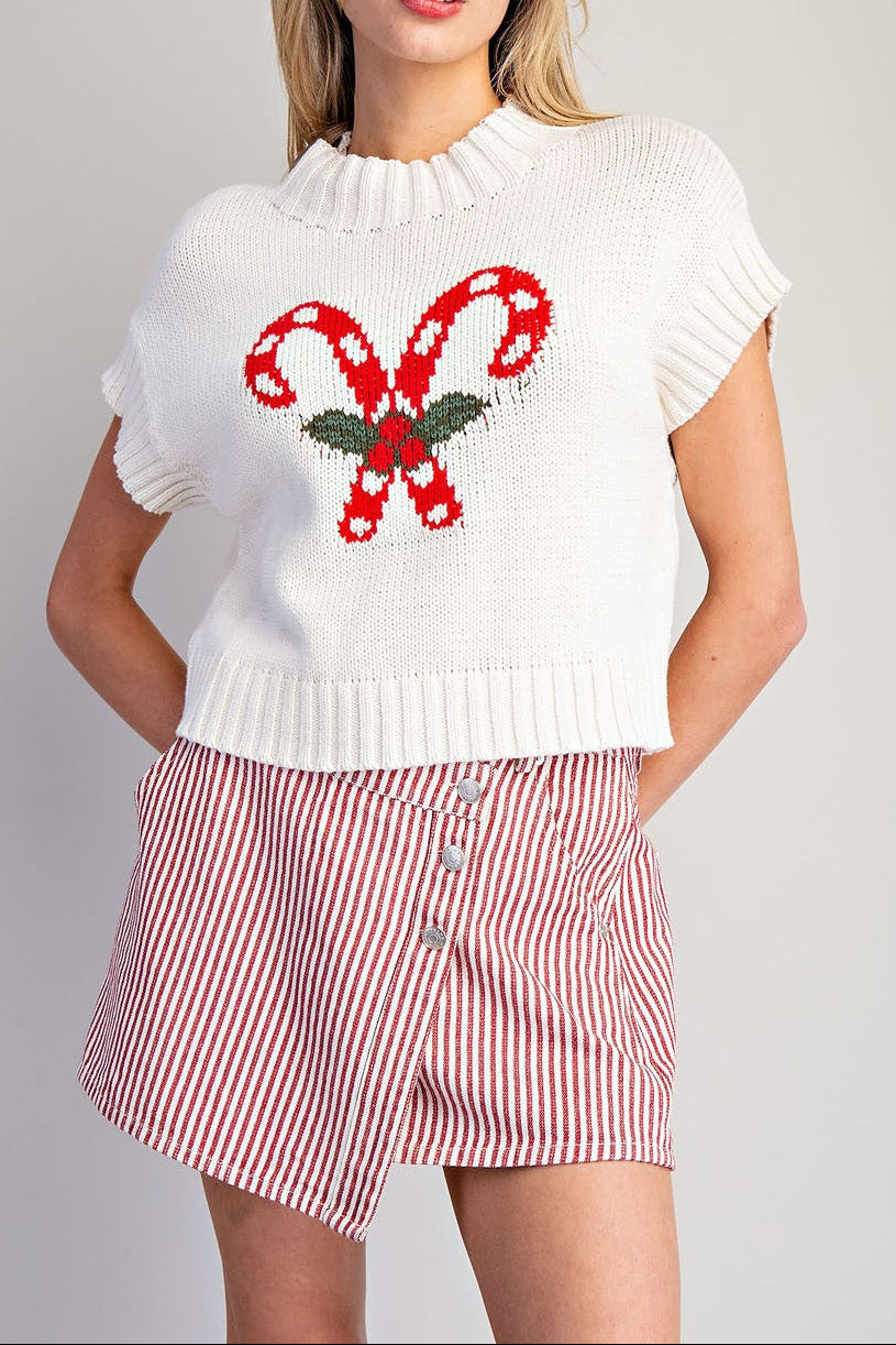 Woman wearing a white sweater with candy cane design and red and white striped shorts on a gray background