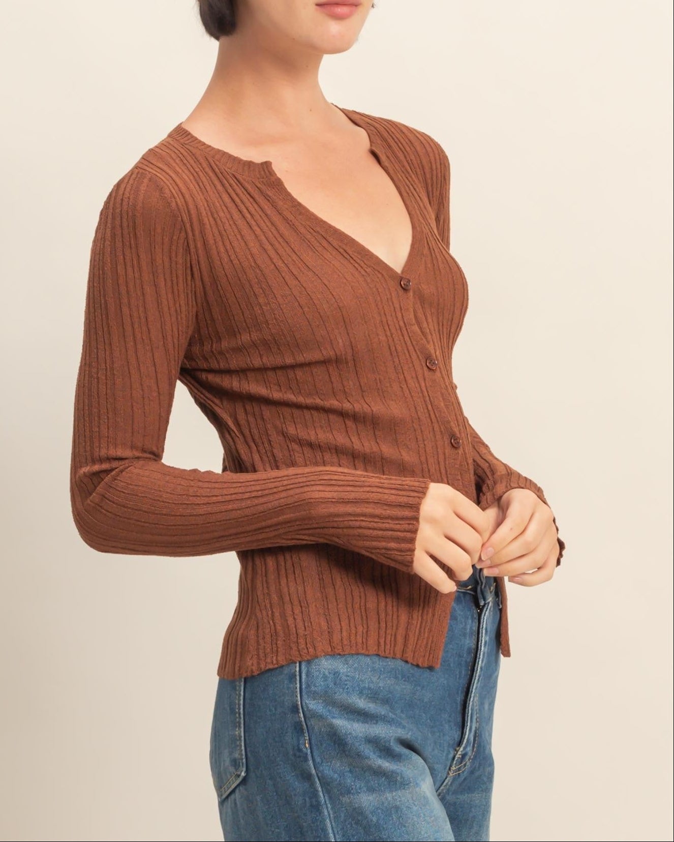Woman wearing a brown ribbed sweater and blue jeans on a beige background