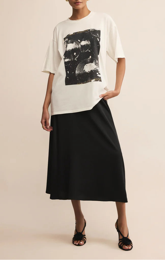 Woman wearing a white oversized shirt with black graphic design and a black skirt on a beige background