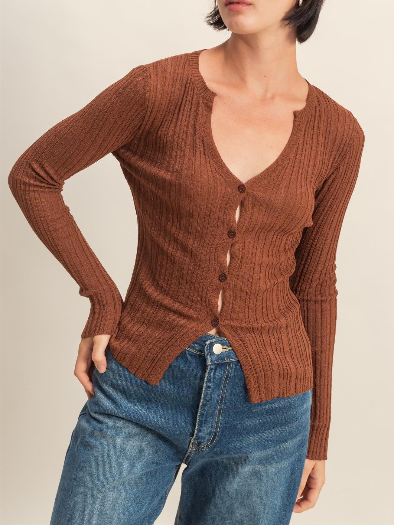 Woman wearing a brown ribbed cardigan and blue jeans on a beige background
