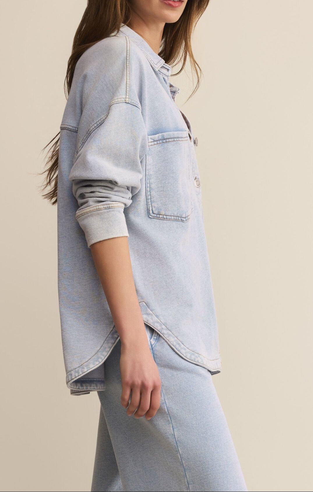 Woman wearing a light blue denim jacket and jeans on a beige background